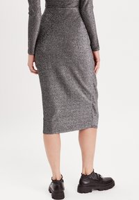 Abito argento struttura, a lunghezza ginocchio, con maniche lunghe e silhouette aderente, abbinato a scarpe nere chunky con una cintura decorativa.