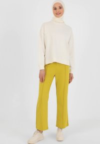 Crème sweatshirt, losse pasvorm, ribbelzoom; gele broek, rechte pijpen, zijsplitten. Model draagt beige sneakers. Eenvoudig, modern ontwerp.