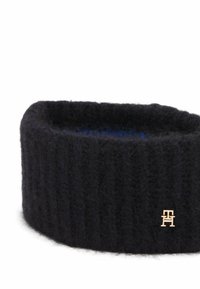 Bandeau tricoté noir en laine douce, avec une texture côtelée et un petit accent logo doré sur le côté.
