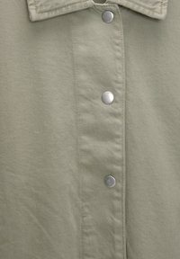 Overhemd met knopen van zachte, lichtgroene stof met een visgraatstructuur, voorzien van zilveren drukknoopsluitingen en een kraag.