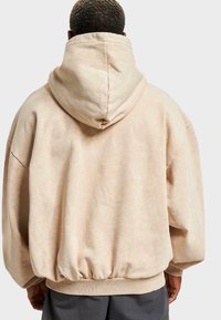 Sudadera beige de gran tamaño con capucha ajustable con cordón, puños y dobladillo acanalados, y tejido suave y texturizado. Ligeramente ajustada en la cintura.