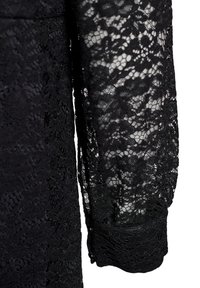 Čierna čipkovaná blúzka s dlhými rukávmi, prepracovanými kvetinovými vzormi a texturovaným povrchom. Rukávy končia detailným manžetovým zakončením.