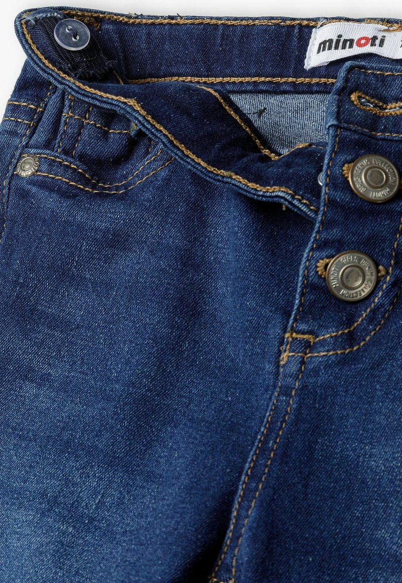 Blaue Denim-Jeans mit goldenen Nähten, zwei metallischen Knöpfen am Bund und einem Etikett mit der Aufschrift "minoti" nahe der Oberseite. Strukturiertes Gewebe.