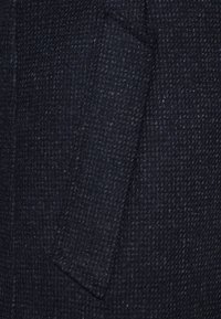 Granatowa tkanina o fakturze z wzorem w kratkę, z pojedynczą kieszenią. Materiał wydaje się wytrzymały i tkany z subtelną głębią.