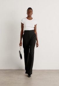 T-shirt blanc ajusté associé à un pantalon noir taille haute, portant un sac à main noir avec une anse en chaîne et des talons noirs.