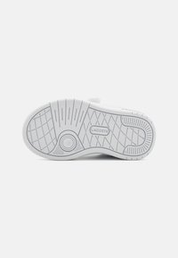 Suola di sneaker bianca in gomma con modelli di grip texturizzati e un logo circolare. Presenta un design flessibile con linee orizzontali e verticali.