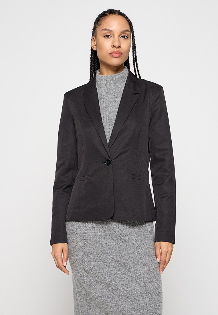Blazer negro con un solo botón, solapas con muescas, dos bolsillos frontales, corte ajustado, combinado con un vestido de suéter gris. Tela suave y ligera.