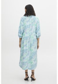Vestido largo de patrones florales en azul claro y verde, con mangas abullonadas, cintura ajustada y falda fluida. Llevado con tacones negros con tiras.