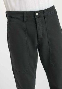 Zwarte casual broeken met voorzakken, riemlussen en een zilveren knoopsluiting, gedragen met een wit shirt.