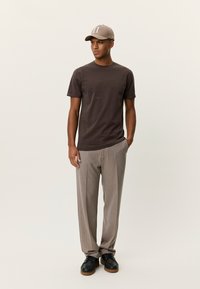 Καφέ κοντομάνικη μπλούζα, γκρι παντελόνι με λεπτές ρίγες και μαύρα παπούτσια. Το καπέλο είναι μπεζ με τον αριθμό "II" μπροστά. Καθαρή, καθημερινή εμφάνιση.