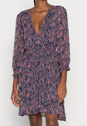 Robe florale navy avec un décolleté en V profond, des manches longues, une taille élastique et unourlet festonné. Présente des petits motifs de fleurs roses et blanches sur l'ensemble.