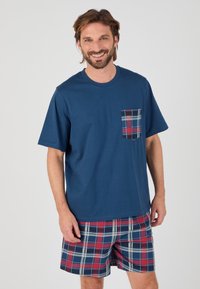 Camiseta de algodón azul marino con un bolsillo de cuadros; pantalones cortos a cuadros en rojo, azul marino, blanco y azul claro. Diseño sencillo, corte relajado, textura suave.
