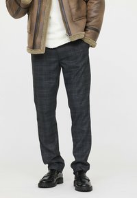 Pantalon à carreaux dans des teintes sombres de bleu et de gris, fabriqué en tissu doux, présente une coupe décontractée et une texture lisse, associé à des chaussures noires.