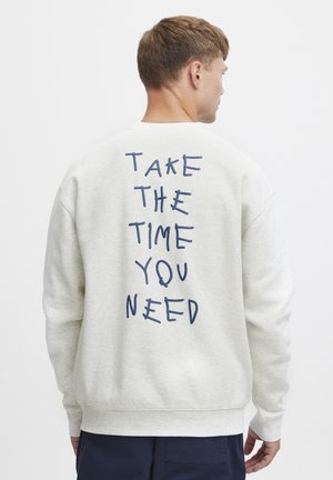 Lys grå sweatshirt med rund hals, prydet med mørkeblå håndskrevet tekst på ryggen: "TAG DEN TID DU BEHØVER." Blødt stof.