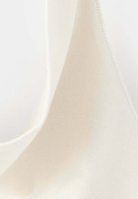 Gros plan d'un tissu blanc avec une texture de tissage diagonal visible et des coutures surpiquées le long du bord.