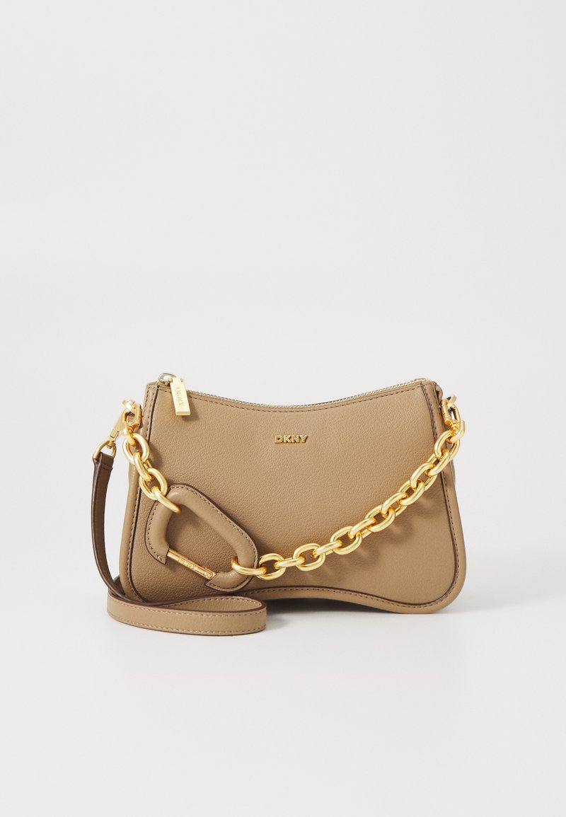 Sac à main en cuir beige DKNY avec une bandoulière chaîne dorée, une petite poignée en cuir et une fermeture éclair sur fond blanc uni.