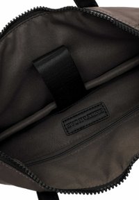 Intérieur d'un tote bag en tissu noir, comprenant une poche zippée et une sangle noire. Texture lisse avec une étiquette noire simple sur le côté.
