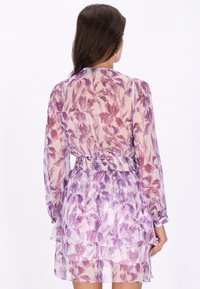 Rochie florală cu mâneci lungi, realizată dintr-un material transparent, având modele cu flori în nuanțe de violet și roz, fustă în straturi și detalii de talie smock. 