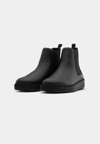 Botas Chelsea pretas feitas de um material suave, com sola baixa e plana e painéis laterais elásticos. Design minimalista com alças de puxar.