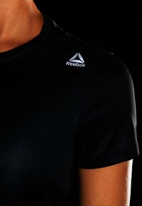 Svart kortärmad träningsskjorta med en slät textur. Har en vit Reebok-logotyp på vänster axel.