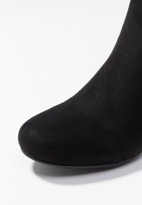 Bottine en daim noir avec un bout arrondi et une texture lisse, présentant une silhouette élégante et un design minimaliste.