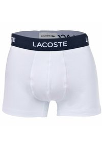 Fehér pamut boxer alsónadrág, sötétkék rugalmas derékkal, rajta a "LACOSTE" logóval. Sima tapintású, illeszkedő forma, rövid szárak, és minta nélküli.