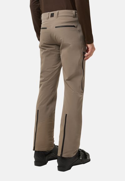 Béžové lyžařské kalhoty s přiléhavým střihem, vysoce kvalitní materiál, kapsy na zip a černé detaily podél boků a lemů.