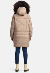 Pufferjas in lichtbeige met een capuchon, voorzien van een doorgestikt ontwerp, lange mouwen en een middellange snit, gecombineerd met jeans en enkellaarsjes.