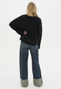 Maglione nero oversize, vestibilità ampia, lavorazione a maglia testurizzata. Jeans blu a gamba larga con orlo grezzo, materiale in denim, risvolti chiari a contrasto.