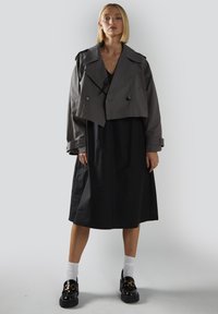 Lyhennetty harmaa takki, jossa on kaksiriviset napit, mustan mekon päällä. Mustat kengät, joissa on kultaketjuyksityiskohta, yhdistetty valkoisten sukkien kanssa.