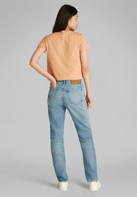 Camiseta de manga corta y corta de color melocotón combinada con jeans de mezclilla azul claro. Los jeans tienen un acabado desgastado y una etiqueta en la cintura.