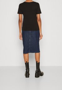 Svart t-shirt med kort ärm kombinerad med en mörk jeanspennkjol med rå kant och en bakre söm, kompletterad med svarta klackade ankelstövlar.