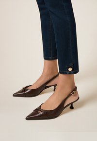 Escarpins slingback en cuir marron avec un bout pointu, des plis à l'avant et des accents dorés. Assortis avec un pantalon en denim foncé et coupé.