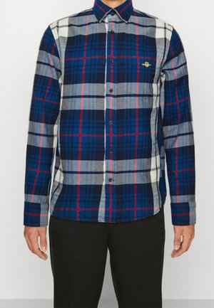 Camisa de cuadros en tela azul, gris y roja con mangas largas, cuello tipo botón y un pequeño logo bordado en el pecho.
