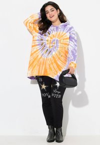 Felpa con cappuccio tie-dye arancione e viola con un motivo circolare e dettagli dorati, abbinata a pantaloni neri con grafiche di stelle argentate.