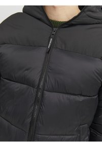 Sort polstret jakke med lynlås foran, hætte og vandrette stikningsdetaljer. Fremstillet af glat, letvægtsstof med mat finish.