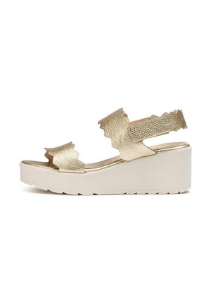 Sandalias de cuña texturizadas en dorado con correas onduladas y suela de plataforma ancha, que presentan un acabado beige suave y diseño sin hebillas.