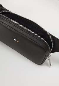 Bolsa transversal de couro preto com superfície texturizada, zíper prateado e detalhe com logótipo. Apresenta um único compartimento para armazenamento.