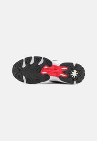 Sole di scarpa sportiva in bianco e nero con un accento rosso in un motivo a onda, battistrada testurizzato per la presa, aree in gomma elevate per il supporto.