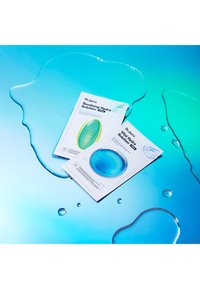 Deux masques de soin Dr. Jart+ sur un fond bleu avec des gouttes d'eau. Les emballages présentent des formes arrondies, des accents verts et bleus, et des étiquettes textuelles claires.