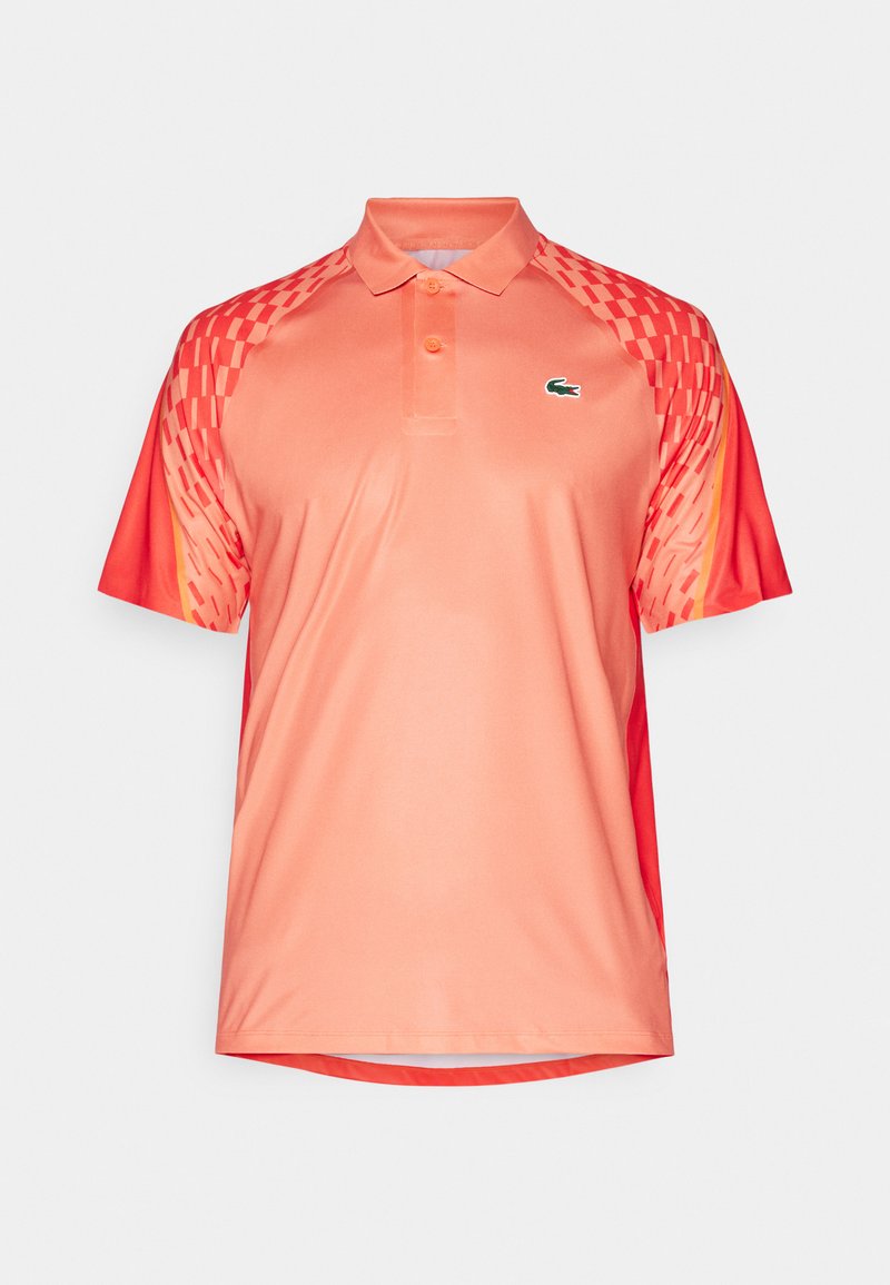 Korallefarbnes Polo-Shirt mit einem schwarzen und roten geometrischen Muster an den Ärmeln. Verfügt über eine Dreiknopfleiste und ein grünes gesticktes Logo.