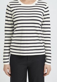 Haut à manches longues à rayures en tissu tricoté noir et blanc, avec un col rond et une silhouette ajustée, associé à un pantalon noir.