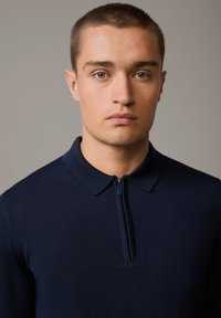 Navy-blaues Poloshirt mit Reißverschluss aus strukturiertem Strickstoff, mit umklappbarem Kragen und kurzen Ärmeln. Slim Fit Design.