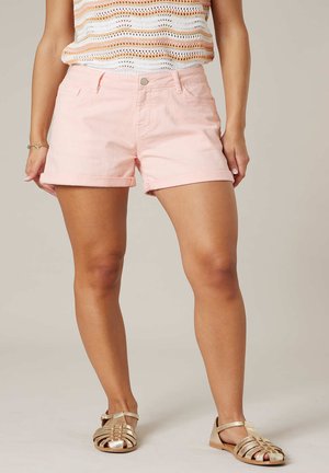 Femme portant un short rose clair à ourlet roulé, un haut multicolore en crochet, des sandales plates dorées à brides et un bracelet à un poignet.