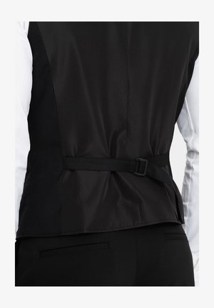 Chaleco negro con una textura elegante, que presenta un diseño aerodinámico, correa trasera ajustable y mangas de camisa blanca en contraste.
