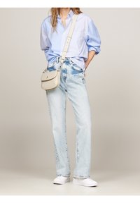 Hellblau gestreiftes Button-up-Shirt, hochgeschnittene helle Jeans und weiße Slipper. Zubehör umfasst eine kleine beigefarbene Umhängetasche.