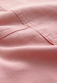 Tissu rose clair avec une surface lisse et légèrement texturée, couture détaillée le long des coutures. Accent sur le drapé doux et la légère brillance.