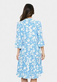 Rochie florală albastră cu modele de flori albe, tiv în straturi și mâneci tip clopot cu trei sferturi. Fabricată dintr-un material ușor.