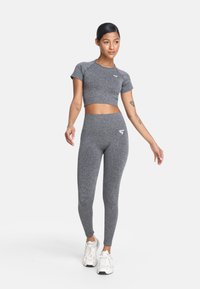 Top corto atlético gris y leggings de talle alto, con un tejido texturizado y un pequeño logo blanco. Combinado con zapatillas blancas.