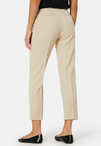 Beige op maat gemaakte broek met een slim fit, voorzien van een middelhoge taille, twee achterzakken en een gladde textuur, gecombineerd met zwarte platte schoenen.